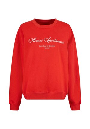 Sarkans džemperis ar garajām piedurknēm, apaļo apkakli, ribotiem aprocēm un apakšmalu. Uz tā ir balta teksta uzraksts: "Aim'n Sportswear" un "Ikdienas devu labklājībai."