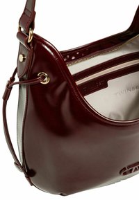 Borsa a spalla in pelle borgogna con finitura lucida, caratterizzata da un ampio interno e hardware color oro. Include una tasca con cerniera e una fodera a strisce.