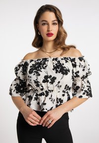 Weiße schulterfreie Bluse mit schwarzem Blumenmuster, puffigen Ärmeln und gerafftem Bund. Kombination mit schwarzen eng anliegenden Hosen.