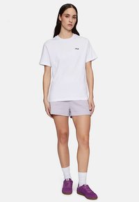 Wit katoenen T-shirt met korte mouwen en subtiel "FILA"-logo. Gecombineerd met lichtpaarse korte broek en paarse sneakers.