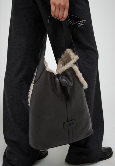 Borsa a tracolla in pelle nera con apertura foderata in pelliccia shearling, dotata di una larga tracolla e logo impresso. Forma elegante e strutturata con finitura opaca.
