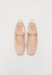 Ballerines véganes rose pâle, avec un bout carré, une bordure froncée élastiquée et une lanière unique. Texture douce semblable au cuir.