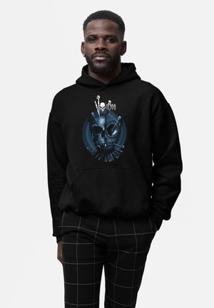 Schwarzer Hoodie mit grafischem Design, das einen Schädel und Voodoo-Nadeln zeigt. Kombiniert mit schwarz-weiß karierten Hosen, die einen lässigen Look präsentieren.
