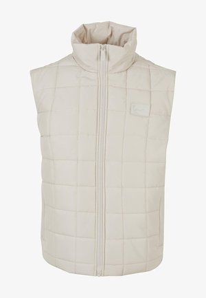 Podložena brezrokavnik v svetlo bež barvi. Ima prešito vzorčenje, visok ovratnik in sprednji zadrgo. Mehka tekstura, brez žepov.