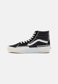 Høye sneakers med en sort semsket skinn-overdel, hvite sømmer, hvite snøringer og en kraftig hvit gummisåle med røde detaljer.
