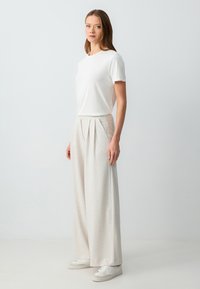 T-shirt blanc à manches courtes associé à un pantalon large beige taille haute avec des plis et un tissu texturé, complété par des baskets blanches.