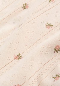 Mjuk rosa stickad tyg med små perforerade mönster och ömt broderade rosa blommor med gröna blad.