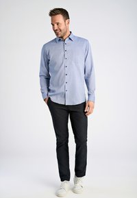 Lichtblauw overhemd met knopen en een geruit patroon, zak op de linkerkant van de borst, gecombineerd met zwarte broek en witte sneakers.