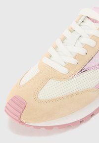 Sneaker featuring a beige suede upper, white mesh panels, and pink accents. Includes white laces and a textured pink sole.