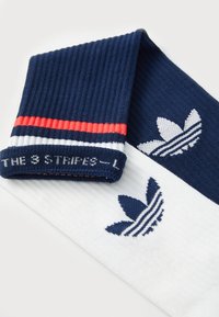 Modré a biele športové ponožky s ryhovanou textúrou, s červeným pásikom a vyšitým logom Adidas v námorníckej modrej. Model označený "THE 3 STRIPES - L".