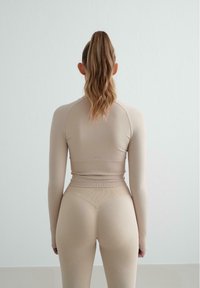 Fitted beige long-sleeve top and high-waisted leggings in a seamless, stretchy fabric, featuring ribbed accents and a minimal design.