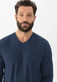 Chemise à col en V à manches longues bleu marine en tissu doux, dotée d'une petite poche sur la poitrine et d'une texture lisse. Design simple et épuré.