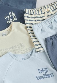 Pile de vêtements pour bébé confortables comprenant des hauts et pantalons bleus, crème et à rayures avec des textes comme "milk club" et "big smiles" dans des tons pastel doux.