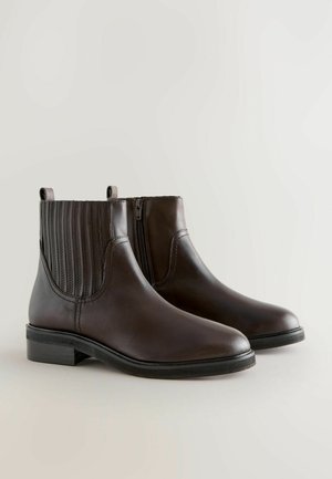 Botas de cuero marrón hasta el tobillo con paneles laterales elásticos y una cremallera lateral, con un tacón bajo y textura suave.