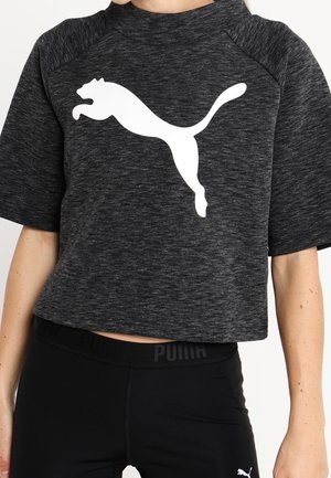 Osoba nosząca ciemnoszarą krótka koszulkę Puma z dużym białym logo Puma i czarne legginsy Puma.