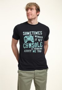Černé tričko s modrým textem a grafikou herního ovladače, se sloganem "Někdy se divím, jestli na mě moje herní konzole také myslí."