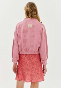 Růžová zkrácená bunda s květinovou výšivkou a elastickým pásem, spárovaná s růžovou sukní s květinovým potiskem. Měkký materiál, dlouhé rukávy.