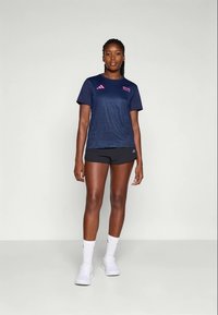 Camiseta deportiva azul marino con acentos rosas, que presenta un sutil patrón de degradado y un cuello redondo, combinada con pantalones cortos negros.
