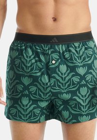 Zelené boxerky s květinovým vzorem, s černým elastickým pasem a zapínáním na knoflík vpředu. Měkká texturovaná látka.