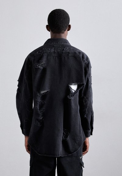 Camasa din denim negru cu un design deteriorat, având multiple găuri mari și margini tocite. Mâneci lungi și un tiv rotunjit completează aspectul.