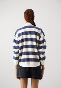 Pruhovaná mikina s vodorovnými pruhy v námořnické modři a krémové barvě, kulatým výstřihem a žebrovanými manžetami, kombinovaná s tmavě denimovou sukní.