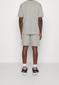 Grå randig kortärmad t-shirt och matchande shorts, tillverkade av mjukt tyg, med vertikala svarta ränder och en avslappnad passform. Svarta träningsskor.