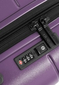 Lila Hartschalenkoffer mit strukturiertem Finish, ausgestattet mit einem Doppelreißverschluss, schwarzen Akzenten und einem Zahlenschloss für zusätzliche Sicherheit.