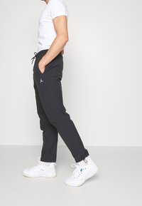 Zwarte joggingbroek met een trekkoord in de taille, zijzakken en een klein wit logo. Gecombineerd met witte sportschoenen en een eenvoudige witte t-shirt.