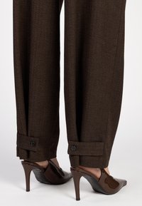Bruine herringbone broek met een tailored fit, voorzien van knoopaccenten bij de manchetten. Gecombineerd met donkerbruine hakschoenen met een slingback.