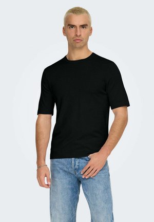 Schwarzes T-Shirt mit kurzen Ärmeln aus weicher Baumwolle, mit Rundhalsausschnitt und lockerer Passform. Getragen mit hellblauen Jeans.