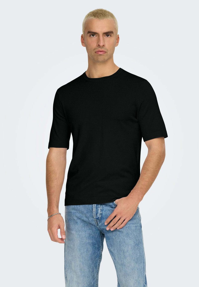 T-shirt nera a maniche corte realizzata in morbido cotone, con collo rotondo e vestibilità comoda. Abbinata a jeans di denim blu chiaro.