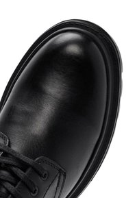 Zapato de cuero negro con acabado brillante, punta redonda y cierre de cordones texturizado. Presenta una suela de goma y un detalle de costura en contraste.
