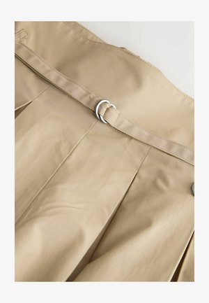 Beežplekiline kangas, millel on sile tekstuur, hõbedase ümmarguse pandla ja vöökihiga. Kangas on kergelt kortsus.