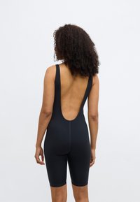 Čierny body s hlbokým výstrihom v tvare U na chrbte, bez rukávov, so zakončením v dĺžke po kolená a hladkou, elastickou textúrou. Má viditeľné švy ako dekoratívne prvky.