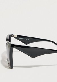 Ochelari de soare negri cu ramă unghiulară și brațe supradimensionate distinctive. Are numele „KARL LAGERFELD” embossat pe lateral.