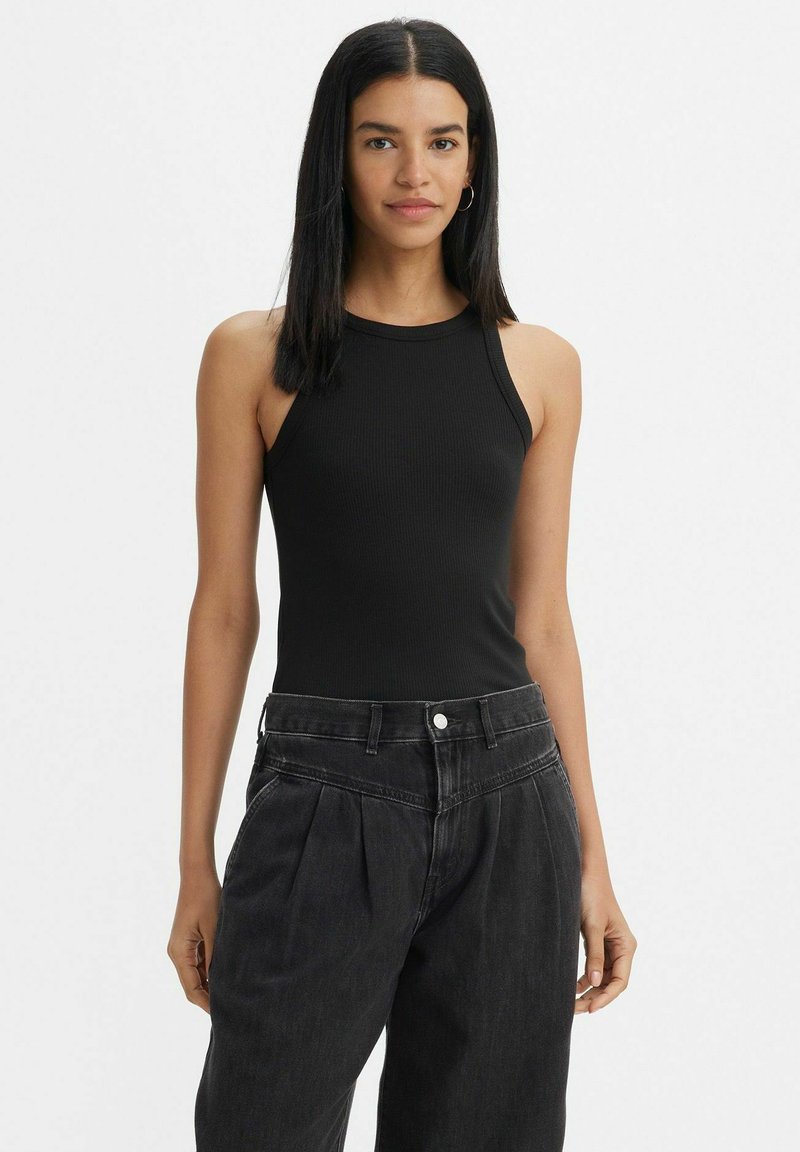 Top aderente nero a costine con scollatura alta, caratterizzato da spalline sottili. Il modello lo abbina a pantaloni in denim scuro a vita alta.