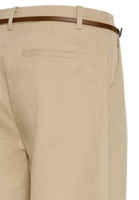 Beige Anzughose mit einem schmalen braunen Ledergürtel, ausgestattet mit einer einzelnen Paspeltasche auf der Rückseite und Gürtelschlaufen.