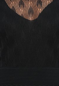 Top negro de punto que presenta un patrón ondulado y un escote en V profundo. La textura es suave con un detalle de cintura acanalada.