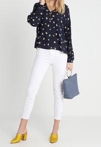 Marinblommig blus, vita cropped byxor, gula klackskor, blå handväska med silverdetaljer, långärmad, knapppydnader på byxorna.