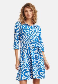 Blau-weiß gemustertes Kleid mit Knopfleiste vorne, Kragen und gebundenem Taillenbereich. Verfügt über dreiviertel Ärmel und einen lockeren Rock.