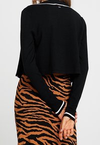 Schwarzer, kurzer Pullover mit langen Ärmeln, ausgestattet mit weißen gestreiften Akzenten am Saum und an den Bündchen, kombiniert mit einem braunen Rock im Tigerstreifen-Design.
