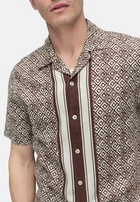 Short-sleeve shirt in brown and cream, featuring a geometric diamond pattern, a pointed collar, and button closure down the front.