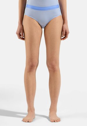 Woman standing barefoot wearing light blue high-waist seamless underwear with a logo on the left hip against a white background.