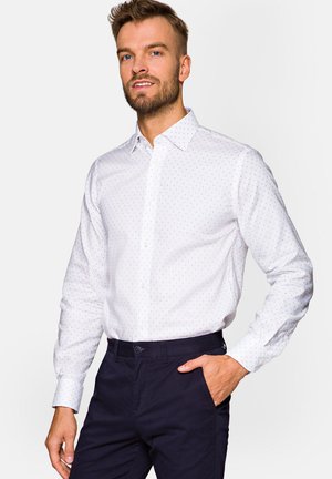 Biała koszula z długim rękawem, pokryta małymi niebieskimi kropkami, z wyrazistym kołnierzykiem, zestawiona z ciemnogranatowymi spodniami. Gładka tekstura materiału.