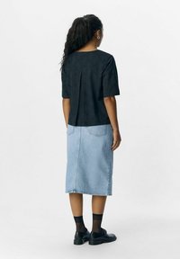 Haut noir texturé à manches courtes avec une coupe ample, associé à une jupe midi en denim bleu clair. Des chaussures noires et des chaussettes à mi-mollet complètent le look.