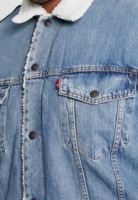 Ljusblå denimjacka med fuskpälskrage, utrustad med två bröstfickor och metallknappar, designad med fransiga kanter och en avslappnad passform.