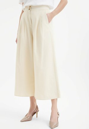 Pantaloni beige a gamba larga con chiusura a doppio bottone e tasche laterali. Realizzati in tessuto testurizzato, presentano una vestibilità ampia e un orlo che arriva a metà polpaccio.