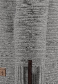 Pull en maille gris avec des rayures texturées, un ourlet côtelé et un patch en cuir marron sur le bas.