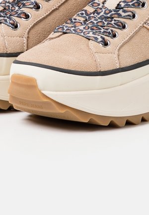 Beige suedet sko med mønstrede snørebånd, hvid gummisål og tydeligt greb. Har en polstret krave og forstærket tåhætte.