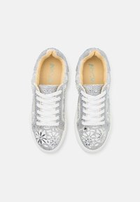 Zilveren sneakers met een bloemen uitsnijd ontwerp, versierd met rhinestones. Witte veters en een lichtbruine binnenzool maken de look compleet.